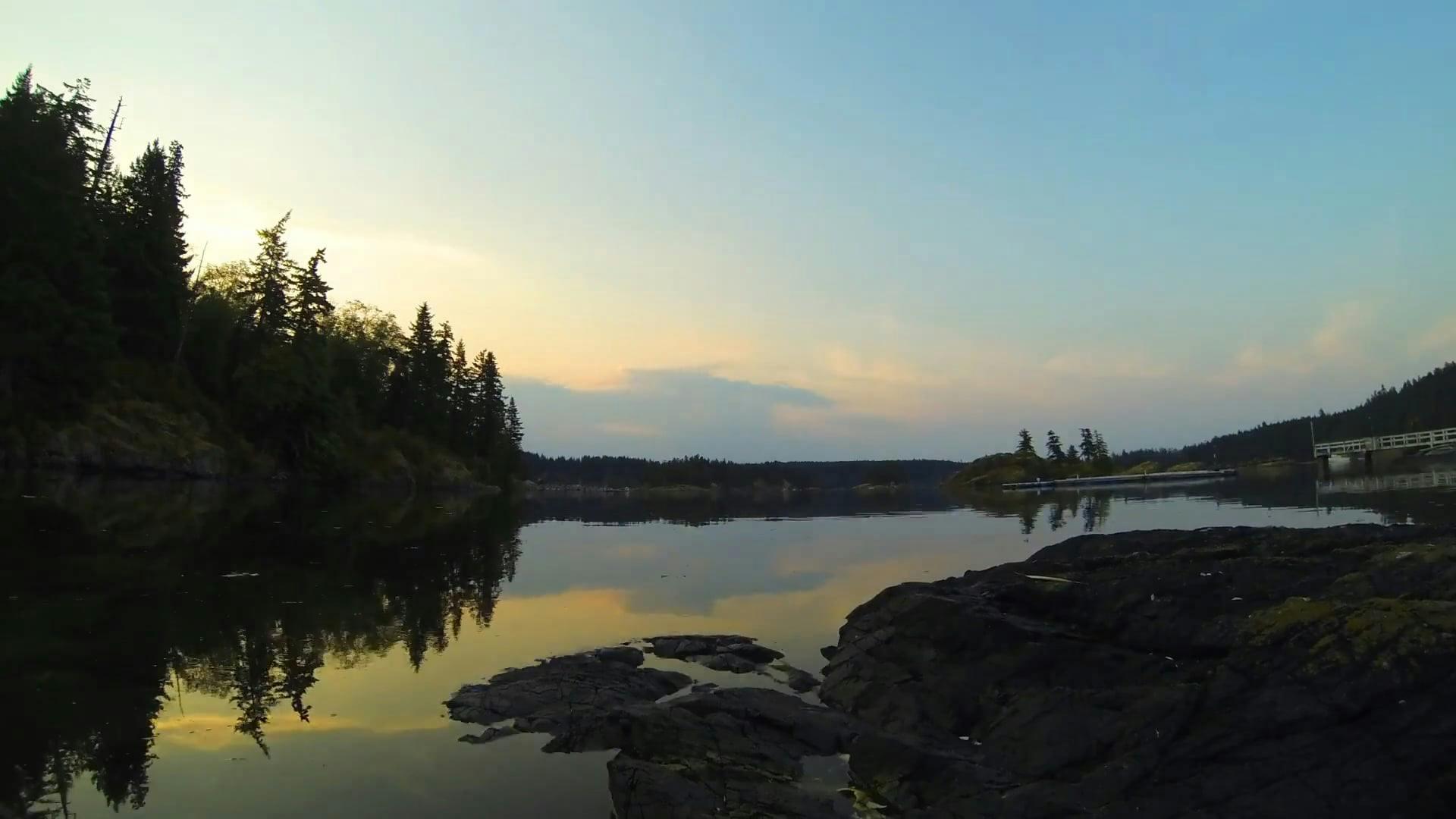 Peaceful Lakeside Scenery With Trees And Rocks At Sunset.